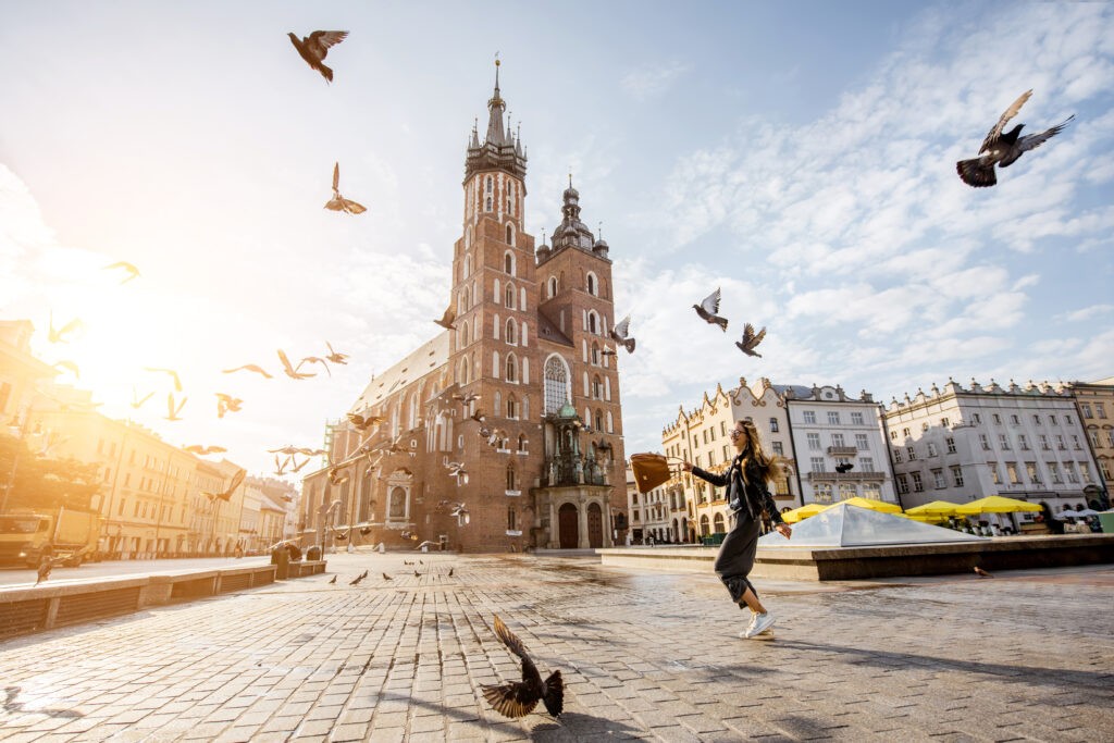 View on the central square and famous st. Marys basilica with pigeons flying during the sunrise in Krakow, Poland